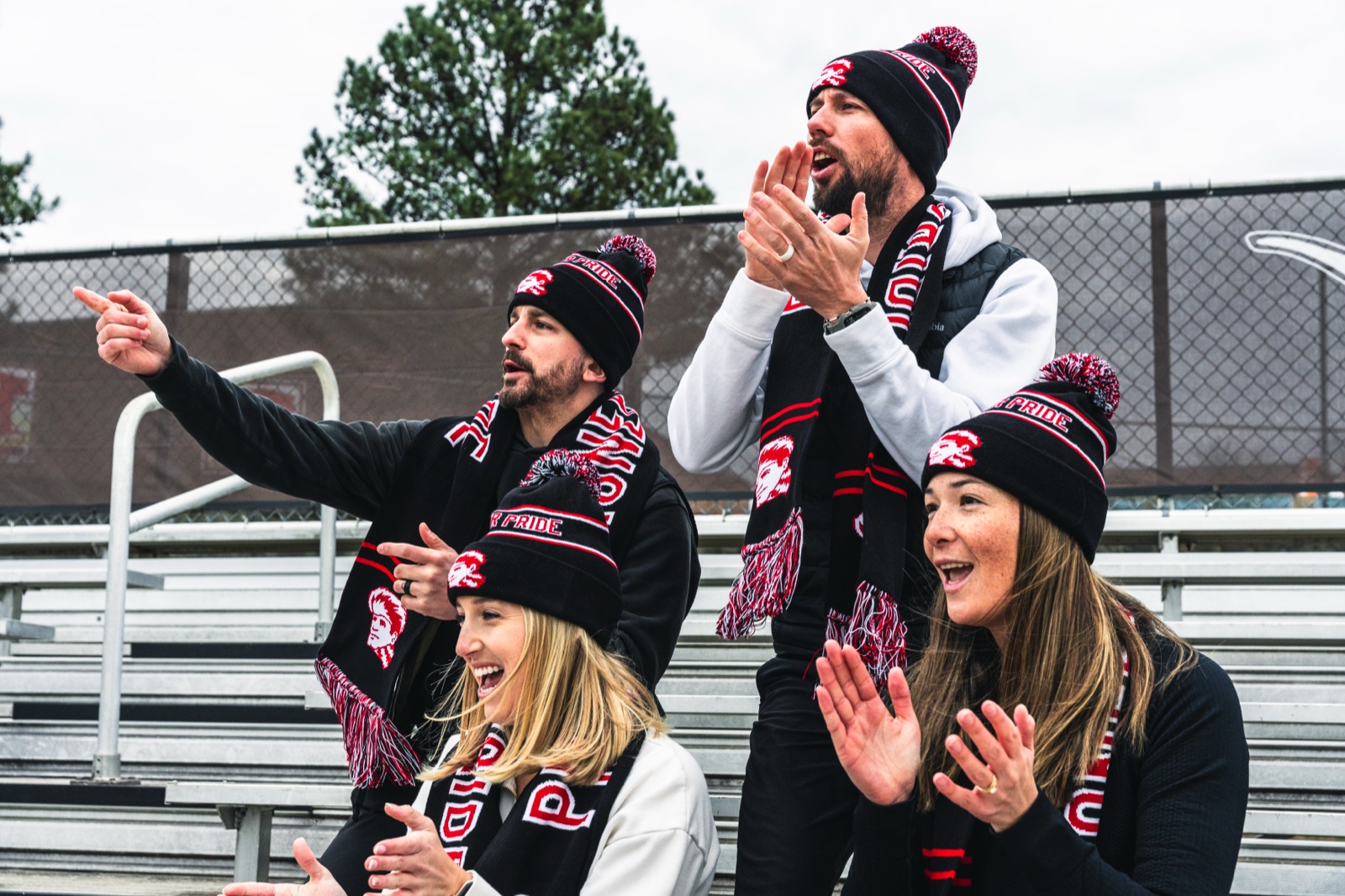 Four fans cheering in matching custom knit pom hats and scarves