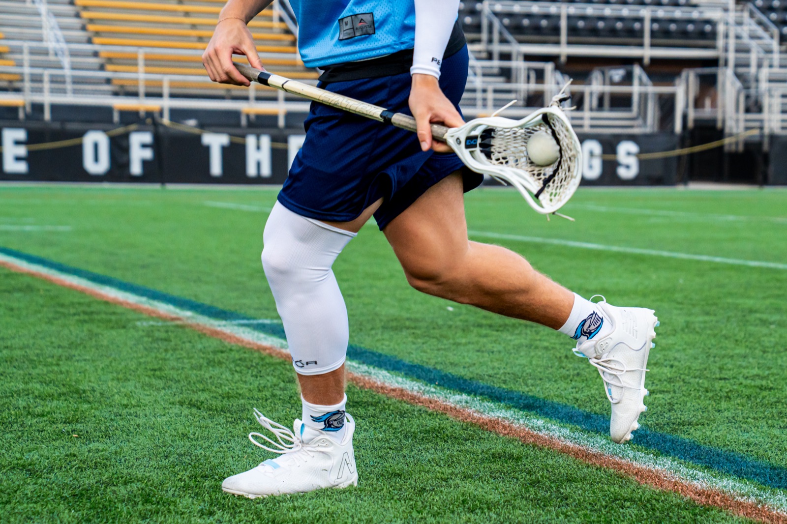 A lacrosse player running with the ball in custom knit socks and a Pear leg sleeve